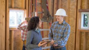 A construction worker with a jard hat talks to a female homeowner.