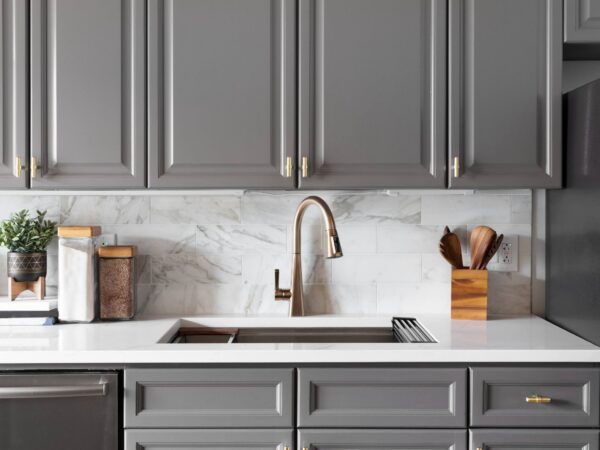 Marble look subway kitchen backsplash tile with gray cabinetry, white countertop, and a brushed metal kitchen faucet.