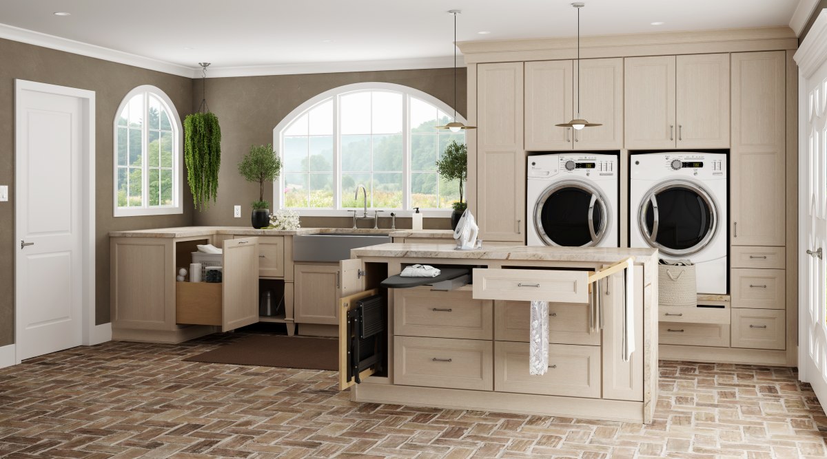 Custom laundry room remodel with light wood cabinetry, raised washer and dryer, folding island, pull out drying rack, ironing board, and utility sink.