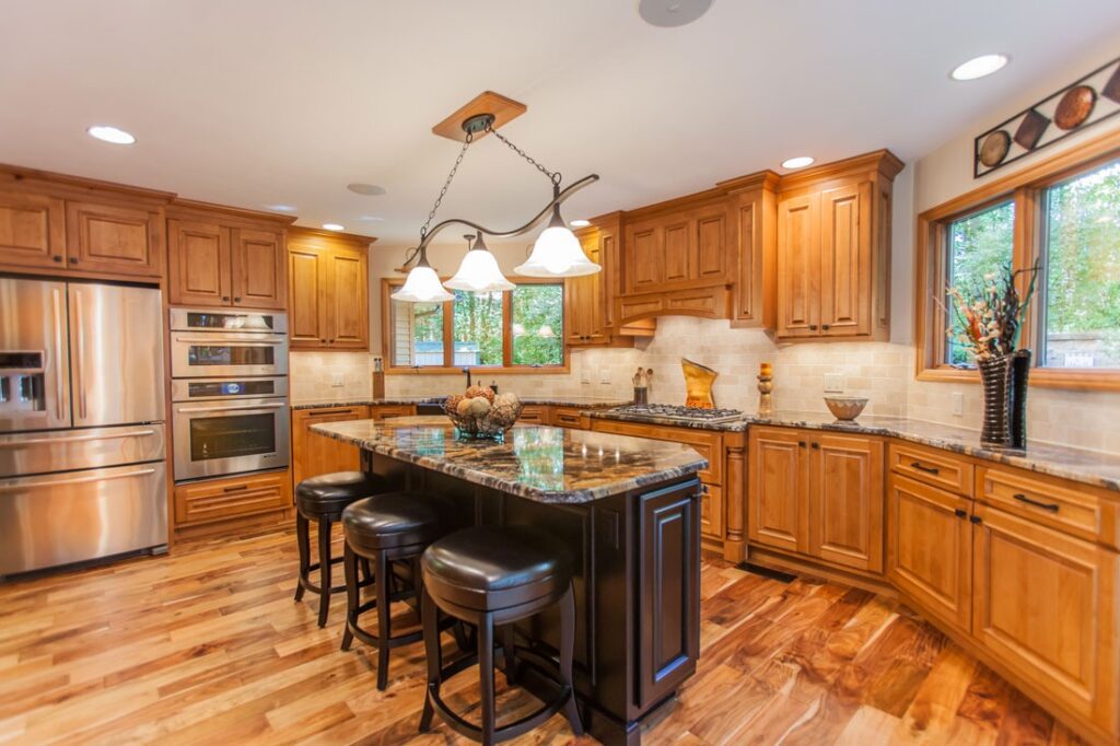 Custom alder wood kitchen cabinets with a caramel stain, dark island, granite countertops, and stainless steel appliances in Mount Pleasant, Iowa.