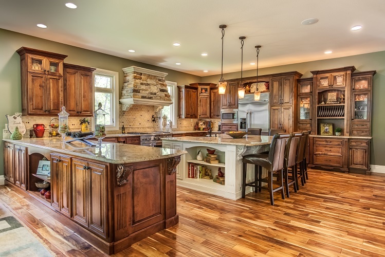 Custom alder kitchen cabinets in a Chestnut stain with Van Dyke Brown glaze, paired with two islands and a stone range hood in Mount Pleasant, Iowa.