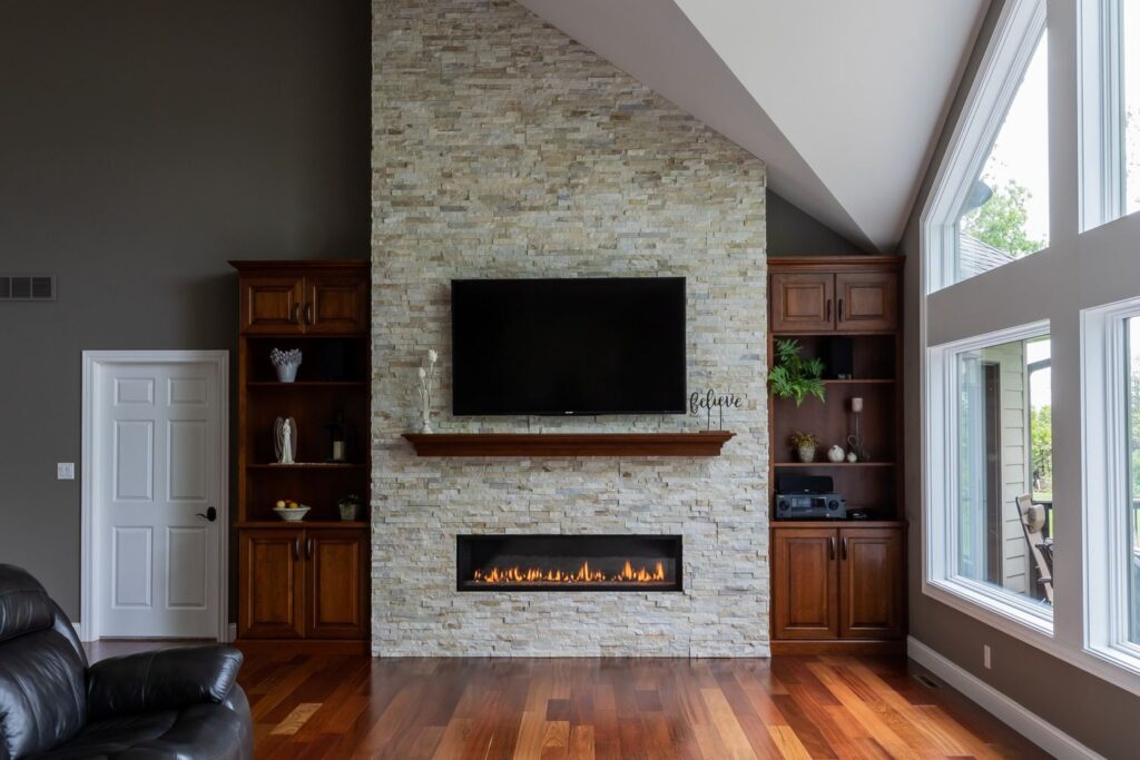 Linear gas fireplace in a tall stone feature wall with custom wood cabinetry and open shelving on both sides.